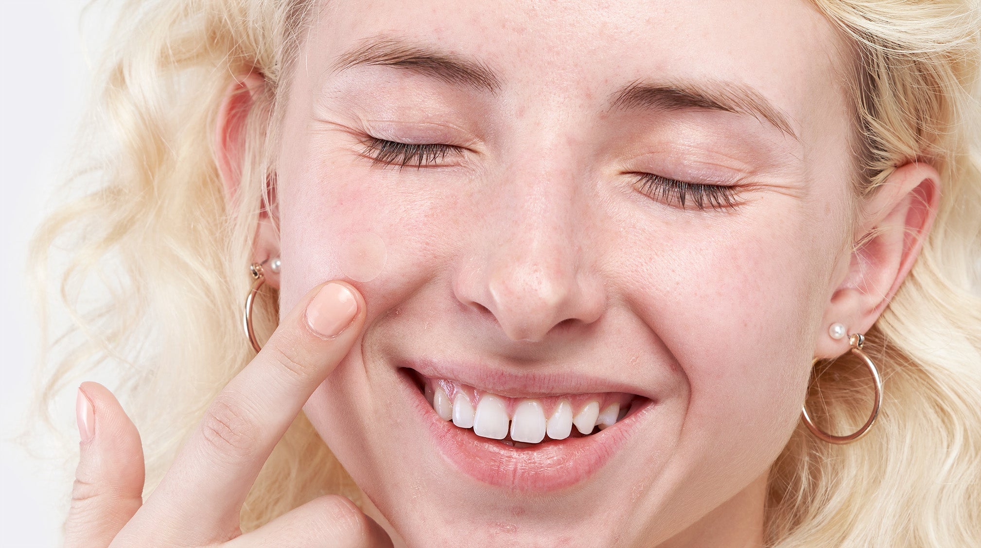 Female applies cream to face whilst smiling.