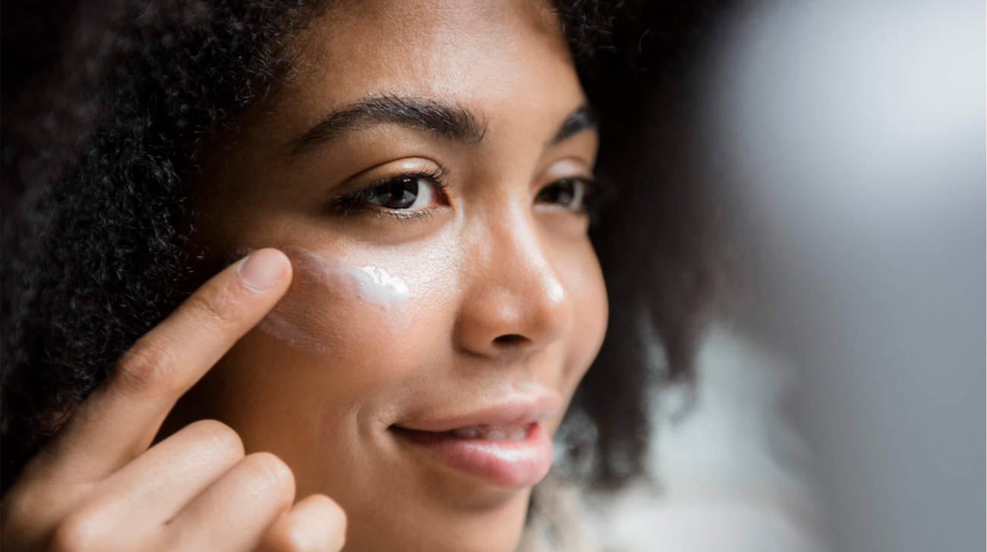 african american woman applying moisturizer on face