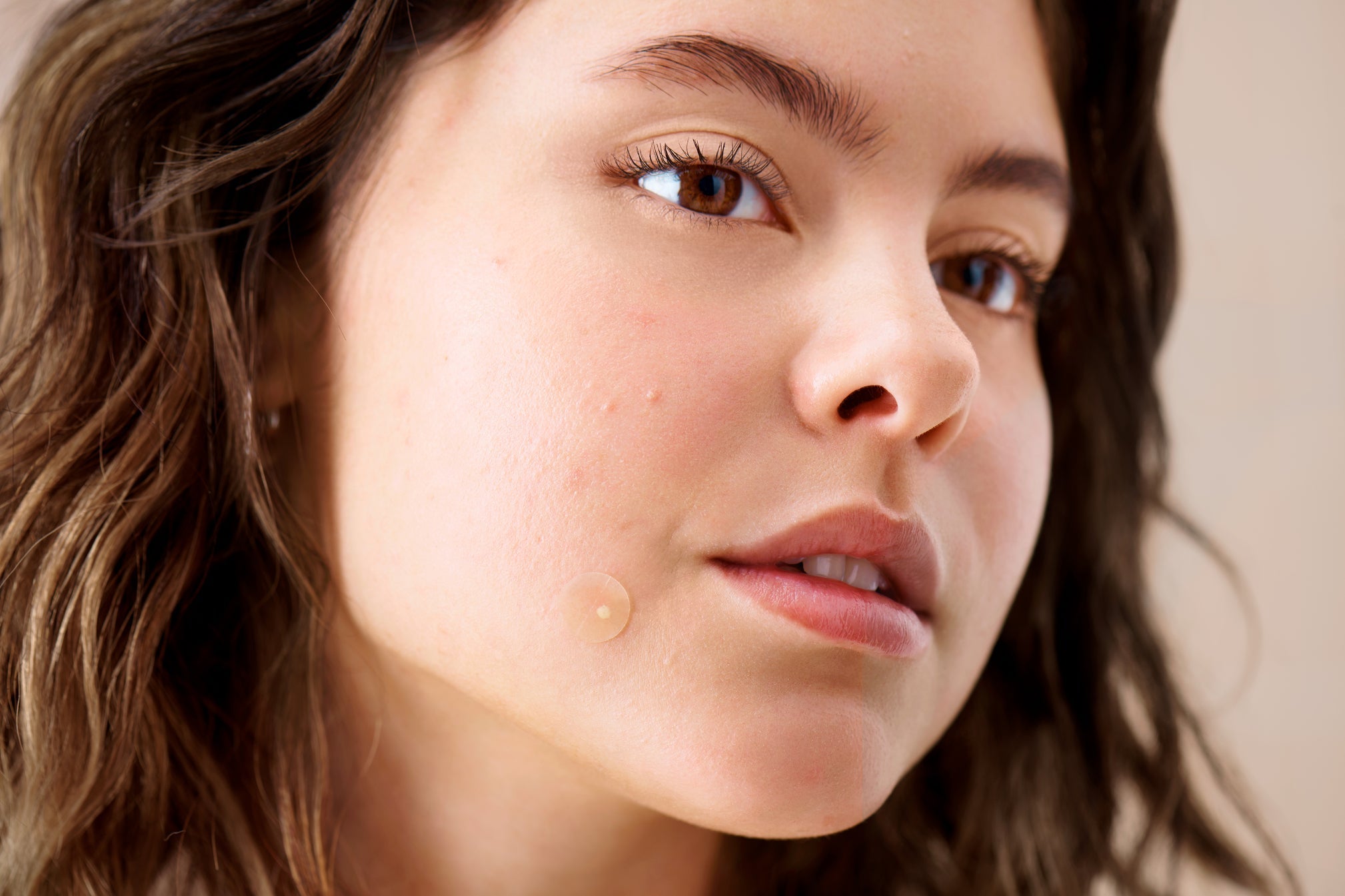 Female wears pimple patch on cheek.