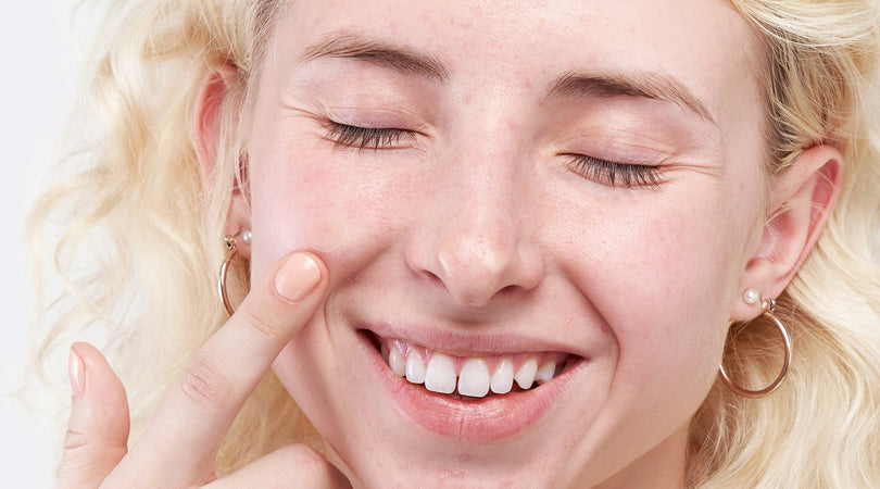 Female applies cream to face whilst smiling.