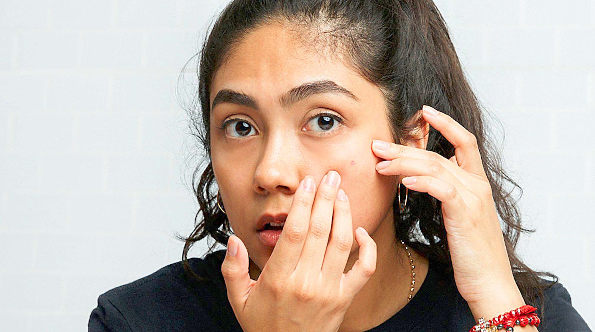 Girl analyzing pimple on face in front of a mirror