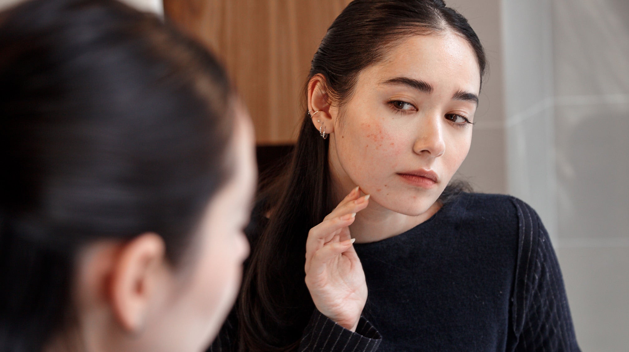 woman examining skin in front of mirror