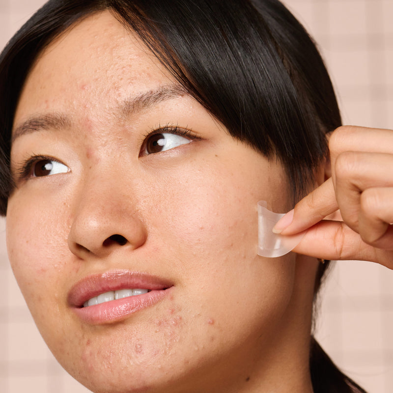 Woman applying a Mighty Patch™ for XL Early-Stage Blemishes patch to her face.