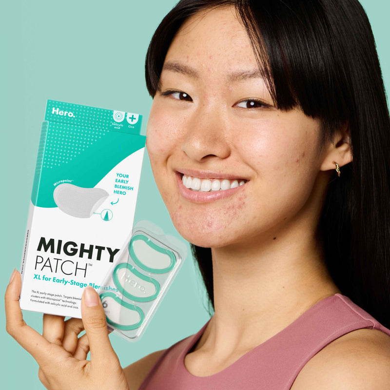 Woman holding package and single tray with three patches of Mighty Patch™ for XL Early-Stage Blemishes.