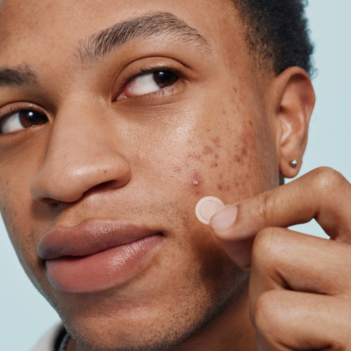 Person with acne holding a Mighty Patch™ Invisible+ patch close to their face.